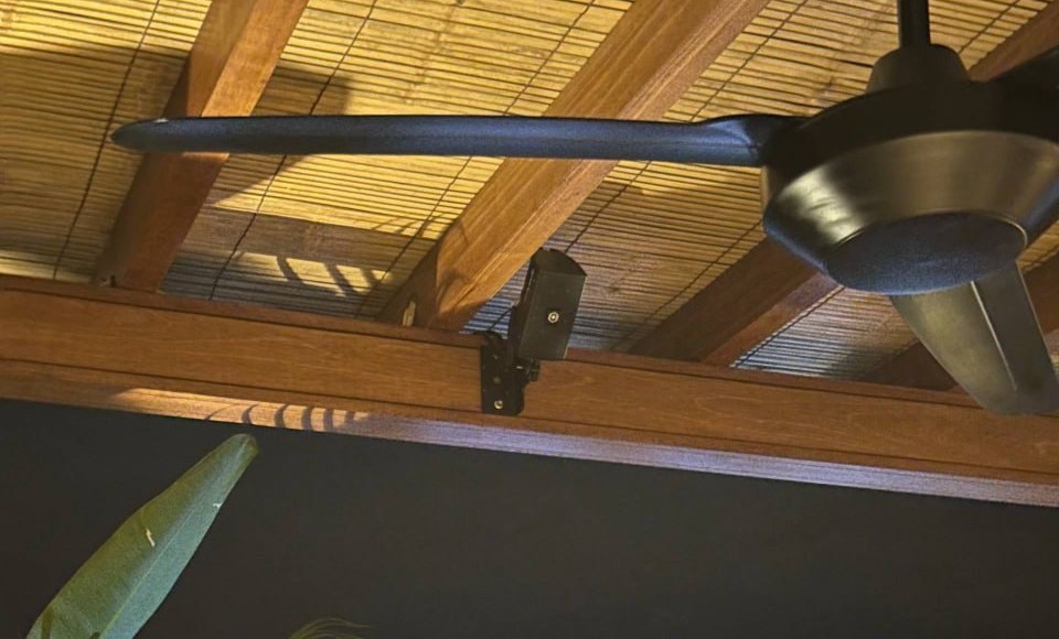 TAS S02 micro-speaker on a timber beam of an Ants Pants gazebo at Family Nest, Uluwatu, under a bamboo-lined roof beside a ceiling fan, photographed at night in January 2026