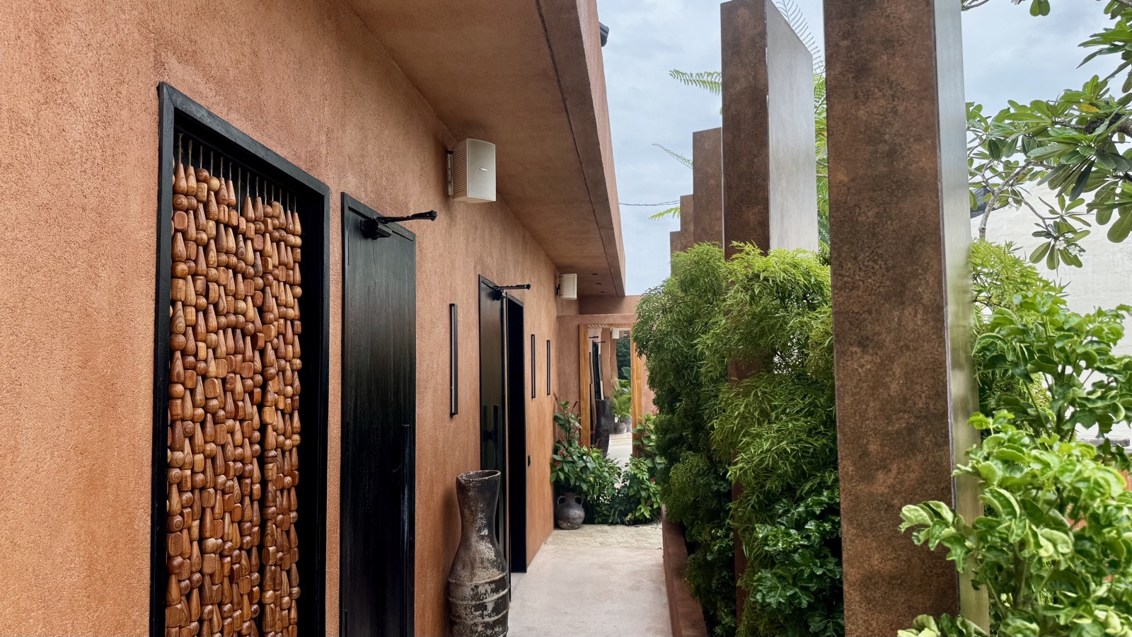 Massage-room corridor at ATMOS with two white Yamaha VS6 surface-mount loudspeakers on the rammed-earth wall above the black doors