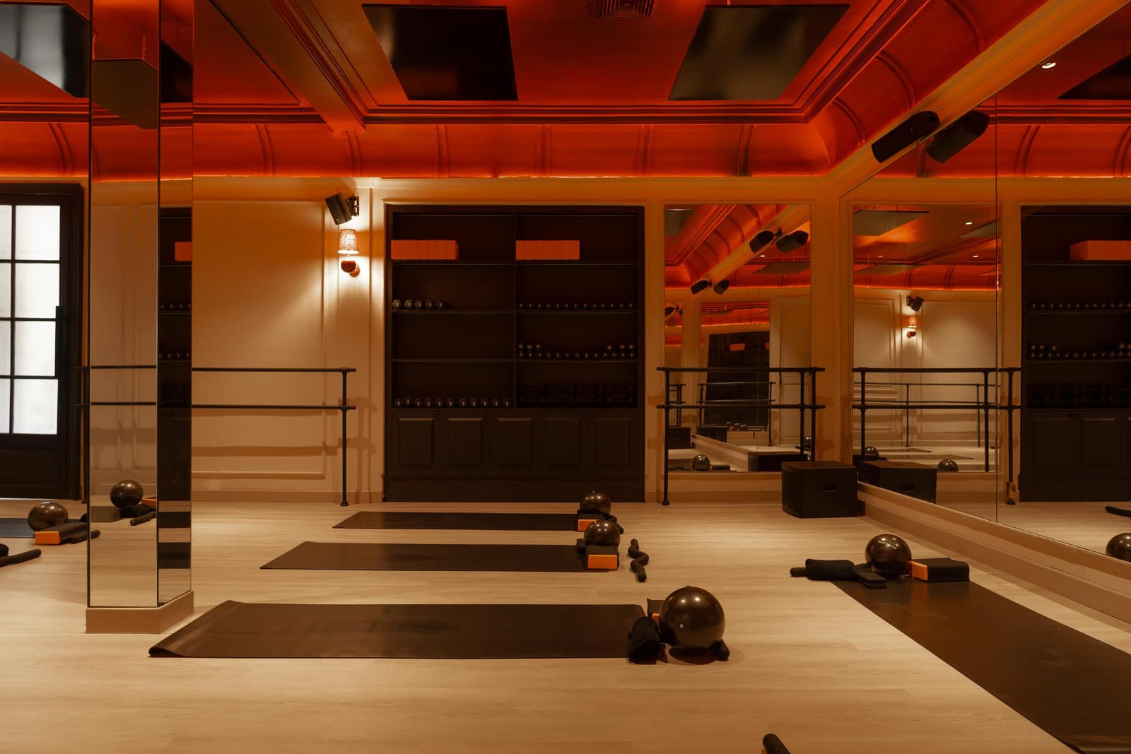 Heated practice room at Heat Space, Bali, lit in warm amber, showing mirrored walls, built-in shelving of props, wall sconces and black yoga mats with sculpt balls and blocks on the timber floor