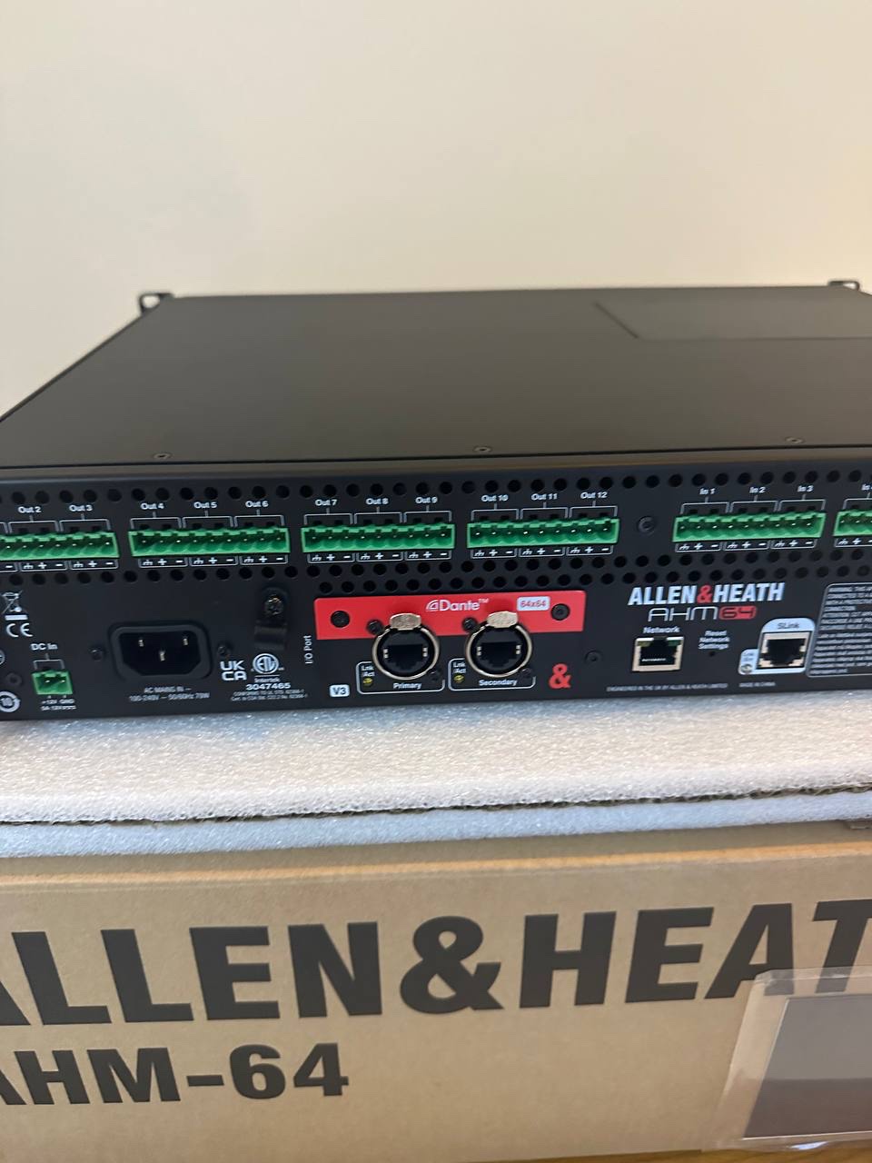 Rear panel of the Allen & Heath AHM-64 during Luna commissioning, 28 December 2023 — red 64×64 Dante card with Primary and Secondary network ports, the processor still on its shipping box