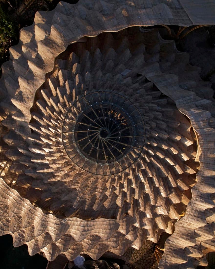 Top-down view into Luna Beach Club's bamboo vortex roof, a carved Fibonacci-spiral funnel converging on a circular skylight