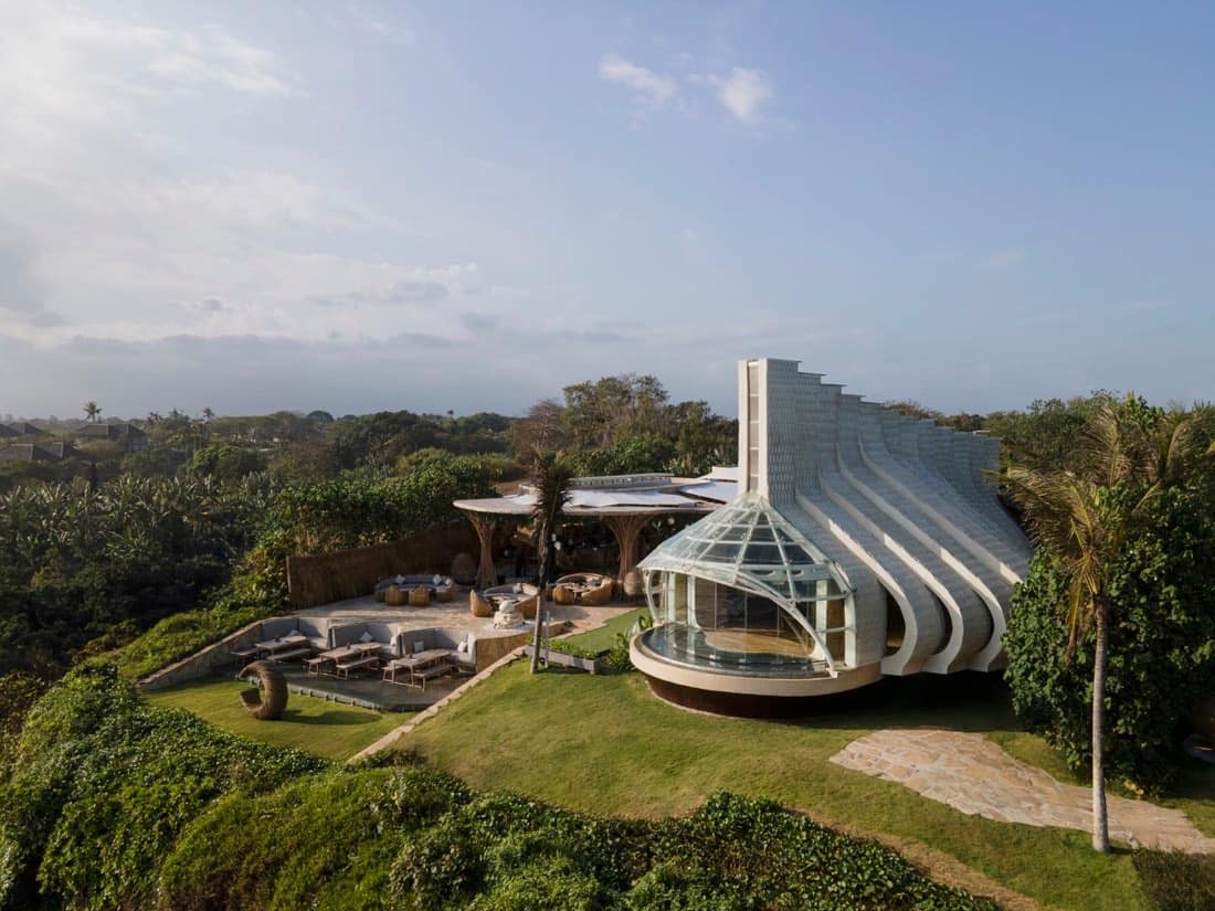 Glass-and-shingle ceremonial pavilion at Luna Beach Club set in green lawns with a shaded lounge