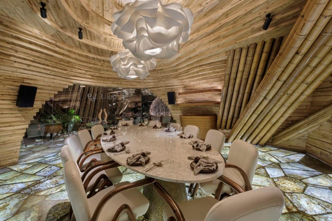 Bamboo-clad private dining room at Luna Beach Club with a round stone table under a swirling timber ceiling and a sculptural pendant light