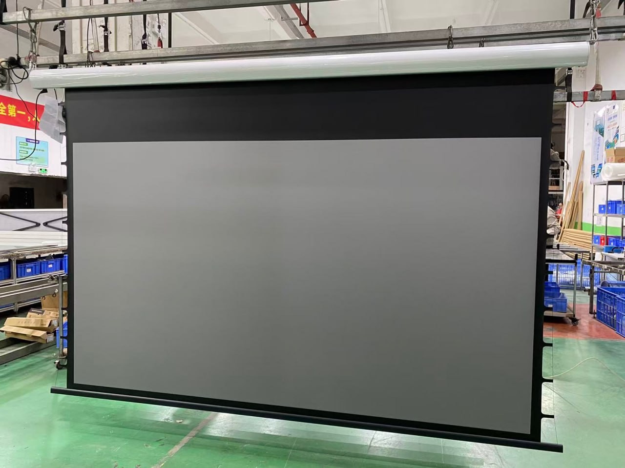Tab-tensioned motorized projection screen with grey Black Crystal ALR fabric, black frame and side tensioners, unrolled for inspection at the factory before delivery to SILK Restaurant