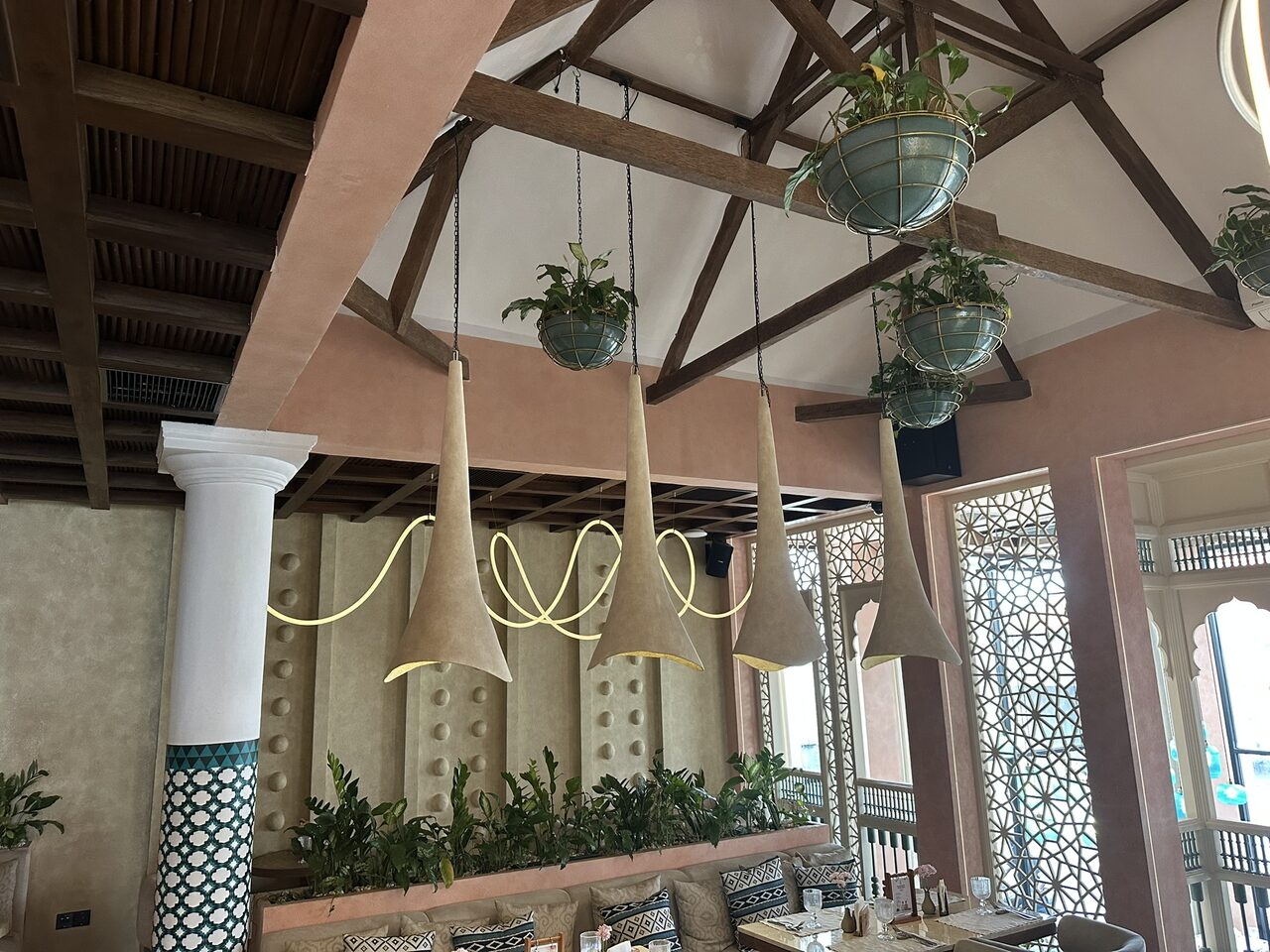 Daytime interior of SILK Restaurant with brick-pink walls, timber roof trusses and hanging pendant lights, a black loudspeaker built into the interior on one of the beams